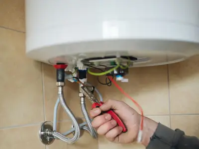 An engineer fixing the connections under a hot water cylinder